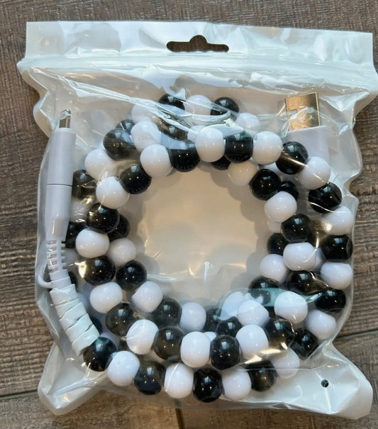 Black and white beaded charger in a clear plastic packaging on a wooden surface.
