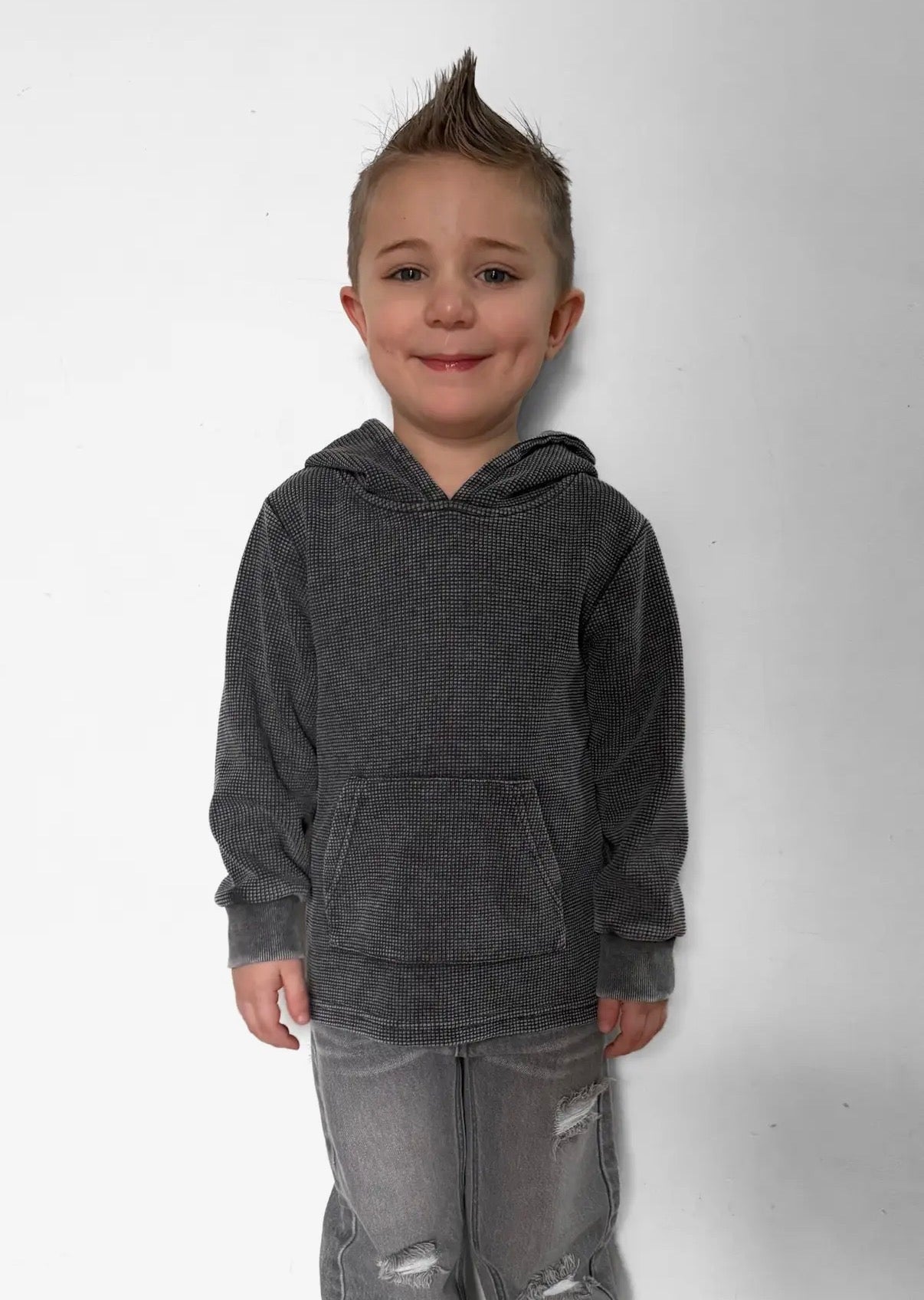 Child wearing a gray hoodie and jeans on a white background