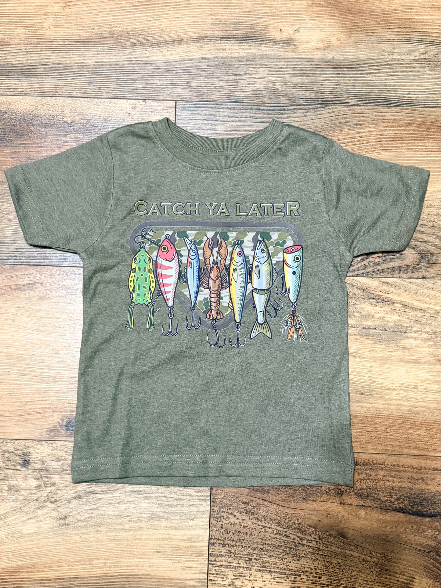 Green t-shirt with fishing lure graphic and 'Catch Ya Later' text on a wooden surface