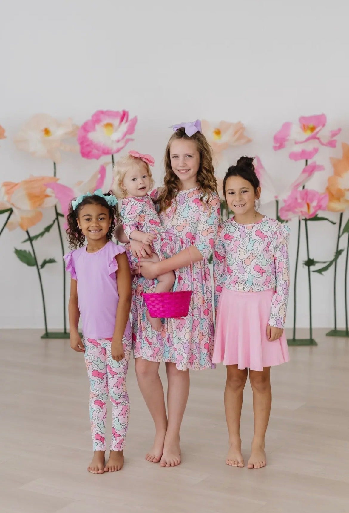 Four young girls in matching floral outfits standing together with a floral backdrop.