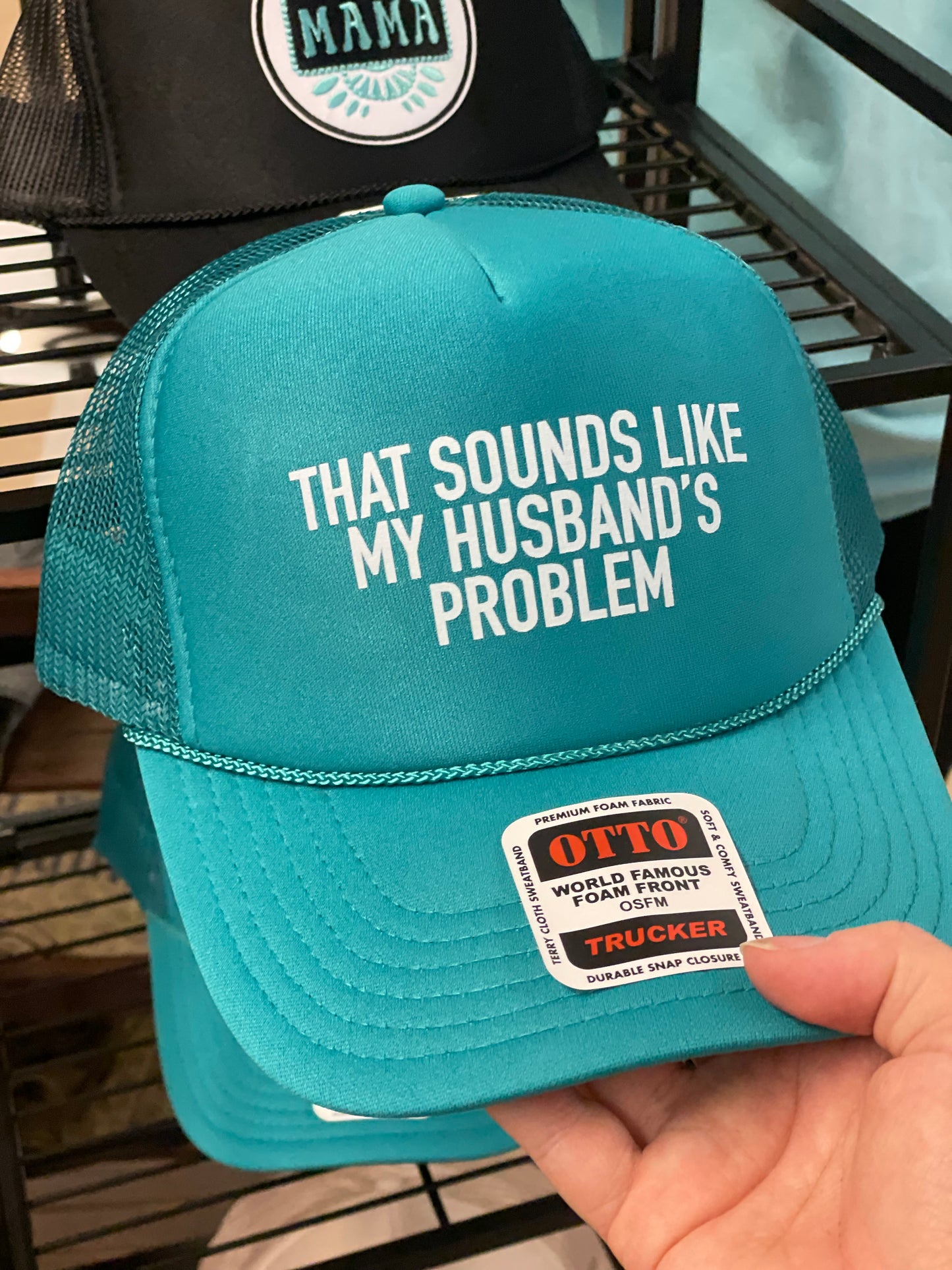 Teal cap with humorous text and Otto brand label held by a hand.
