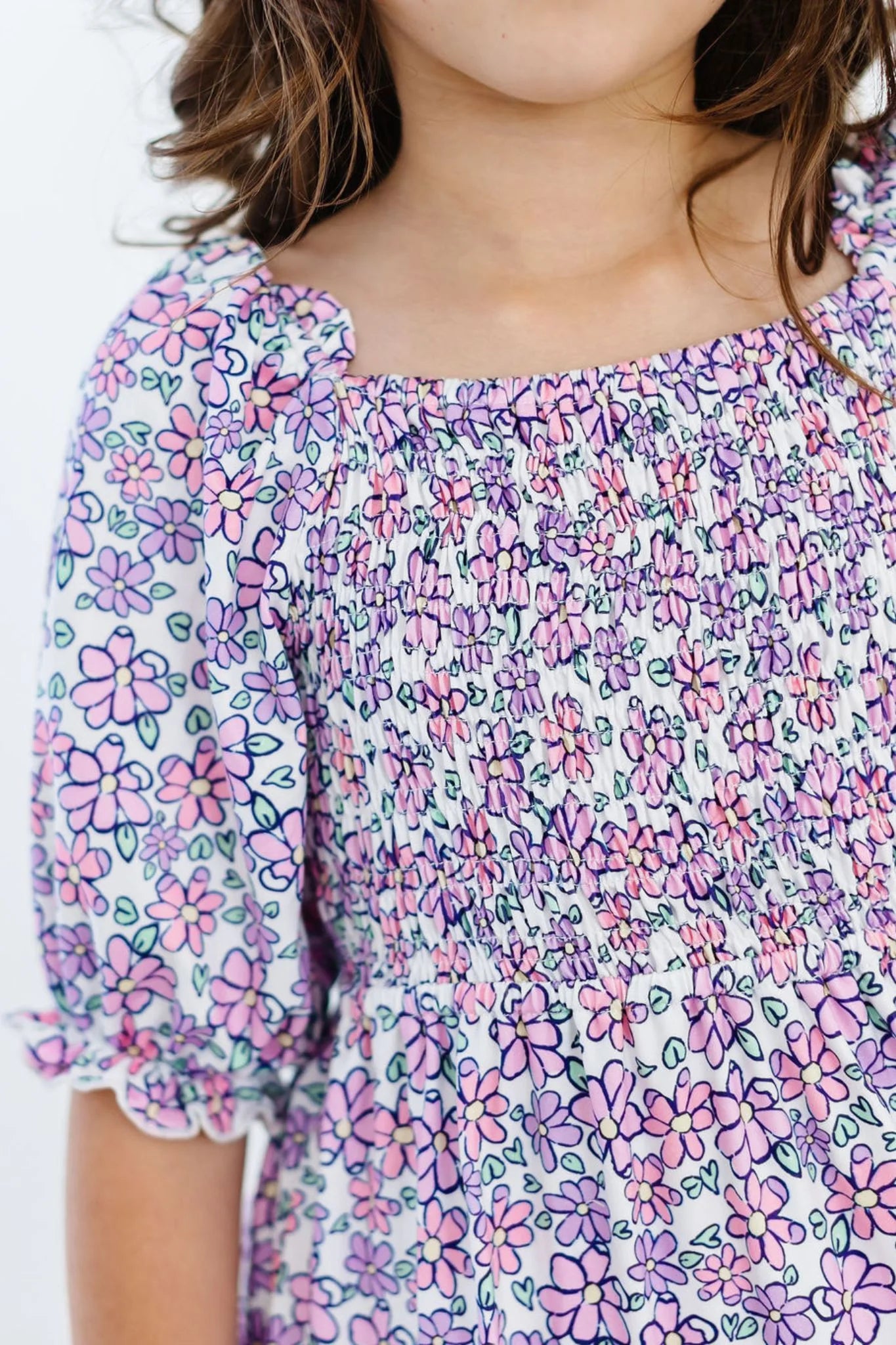 Close-up of a child wearing a floral dress with pink and purple flowers.