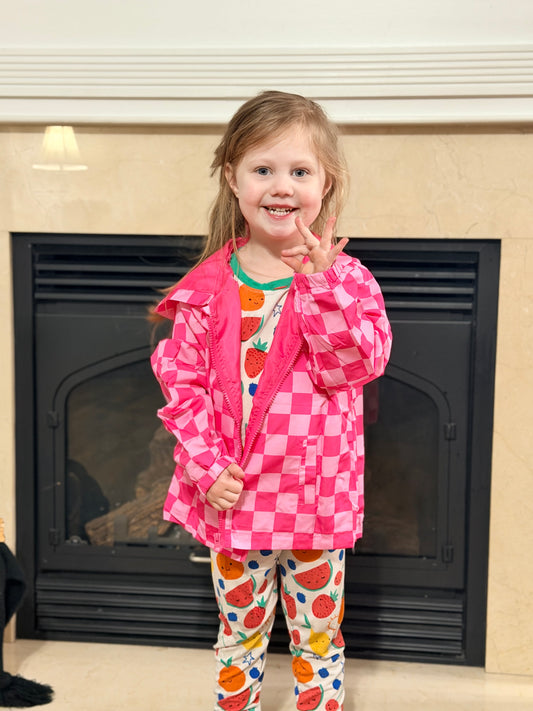 Child wearing a pink checkered jacket and colorful pants in front of a fireplace.