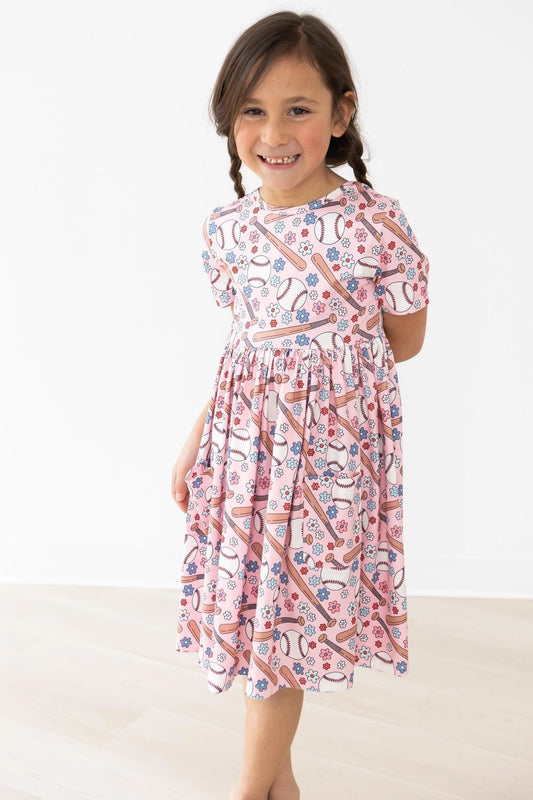 Young girl wearing a patterned baseball dress on a white background