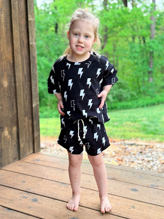 Child wearing a black outfit with white lightning bolts on a wooden deck