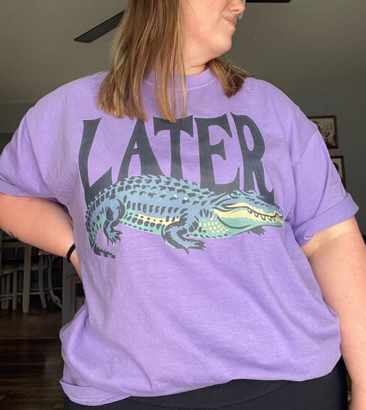Person wearing a purple t-shirt with an alligator graphic and 'LATER' text.