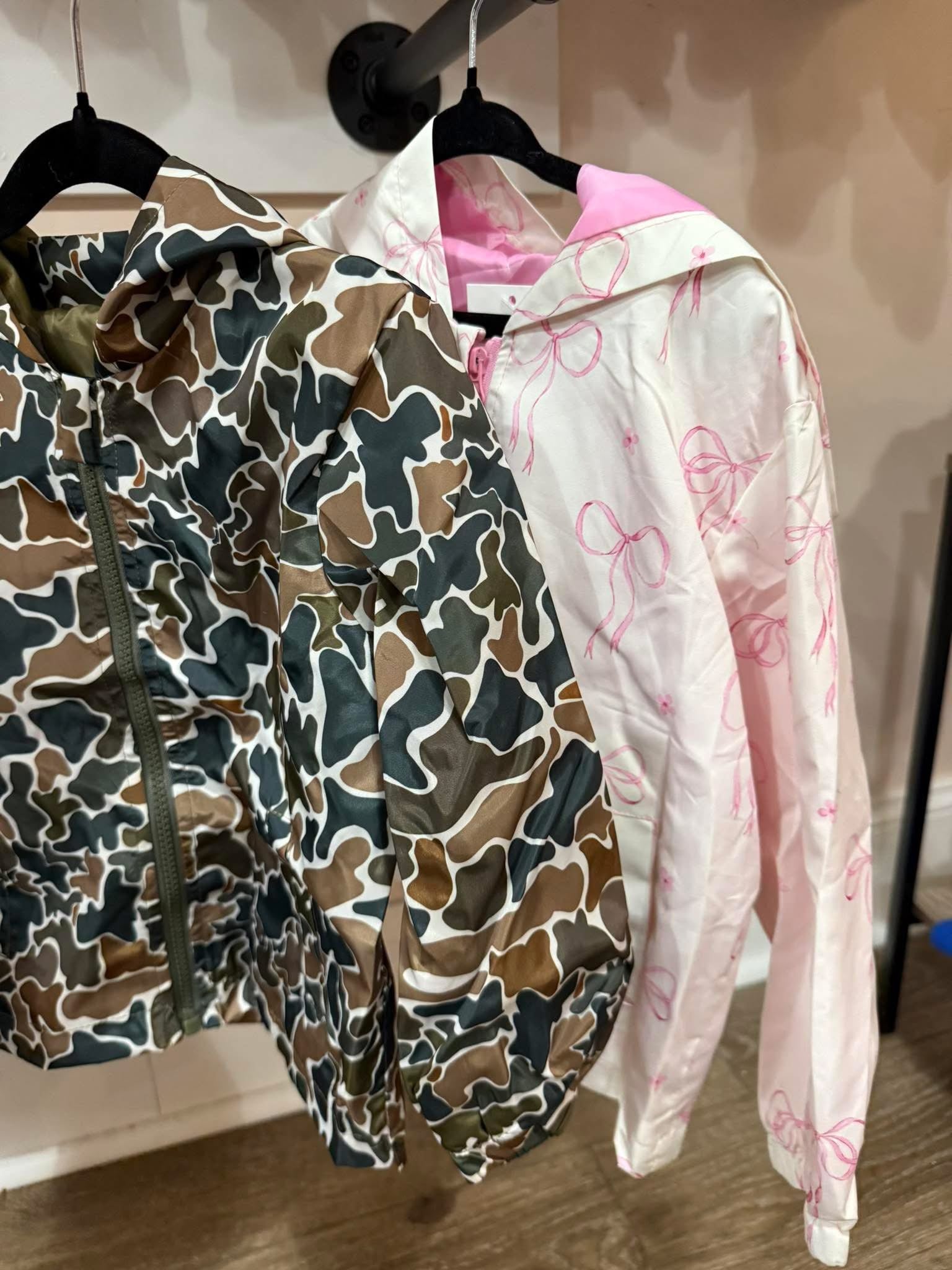 Two jackets, one camouflage and one pink with floral patterns, hanging on a rack.