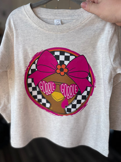 Natural colored long sleeve t-shirt with a graphic of a turkey wearing a pink bow and 'Gobble Gobble' text.