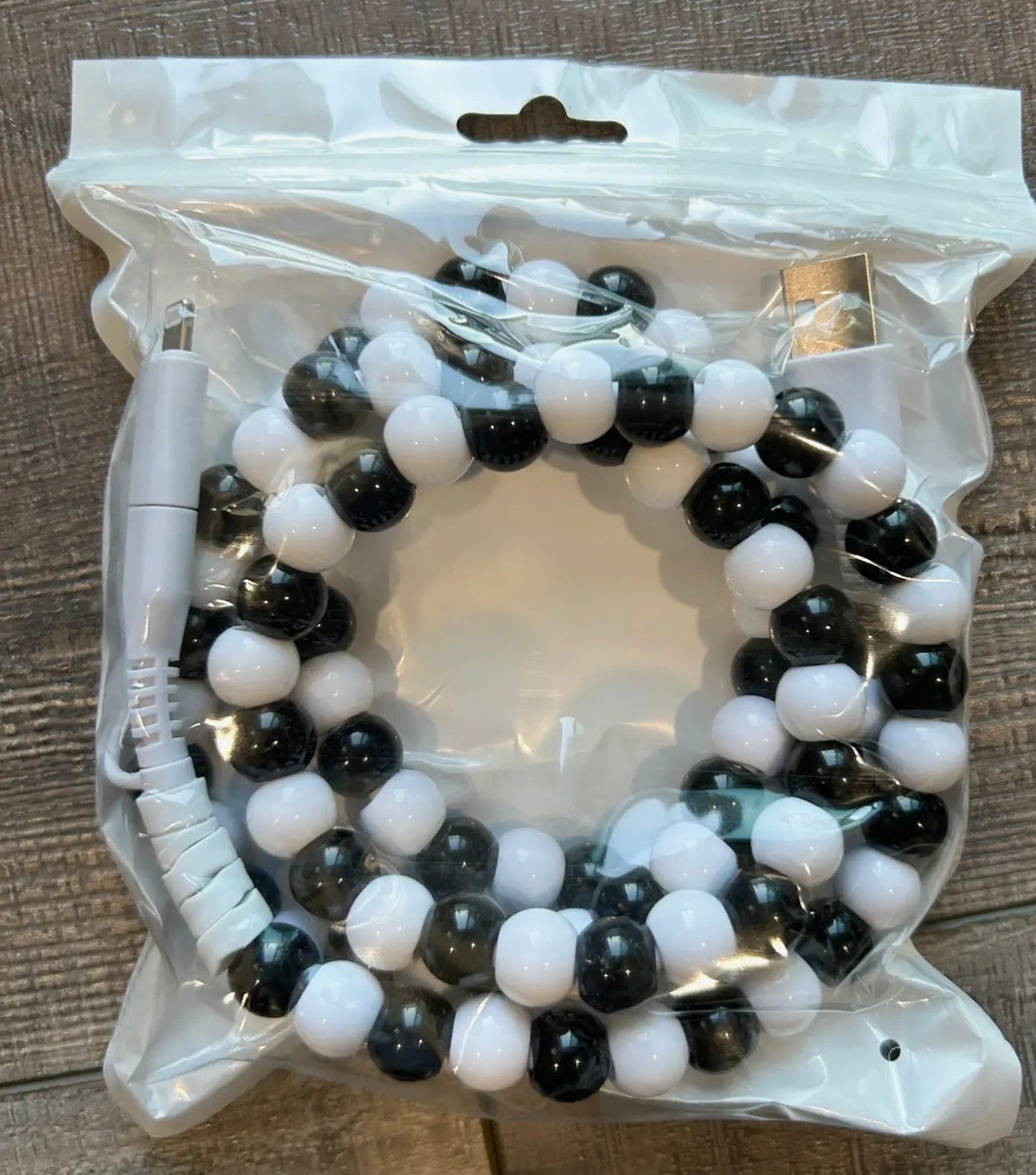 Black and white beaded charger in a clear plastic packaging on a wooden surface.