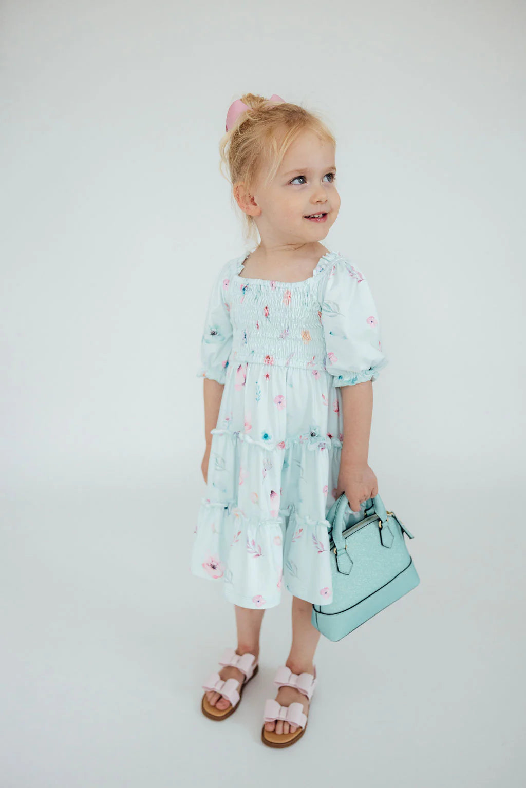 Young girl in a light blue floral dress holding a matching handbag against a white background