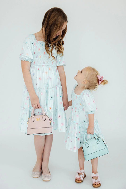 Girls in matching light blue dresses with colorful patterns, holding small handbags.