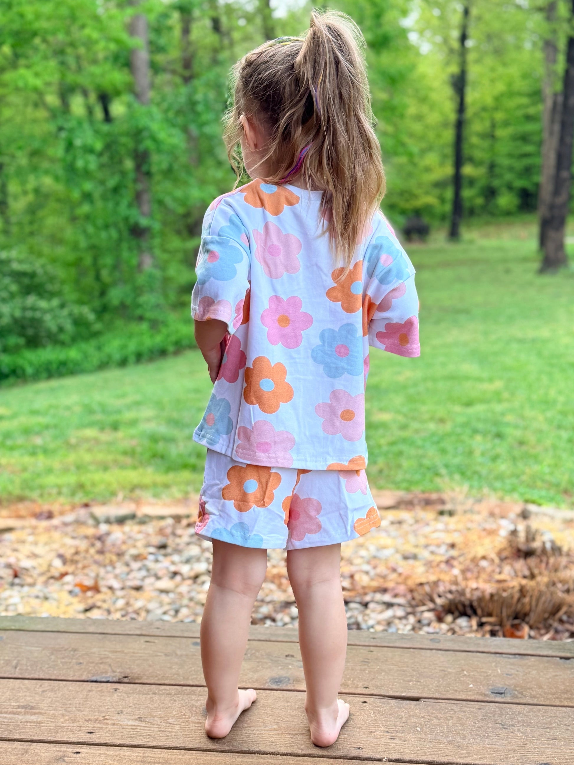 Child wearing a floral outfit standing on a wooden deck with a green outdoor background