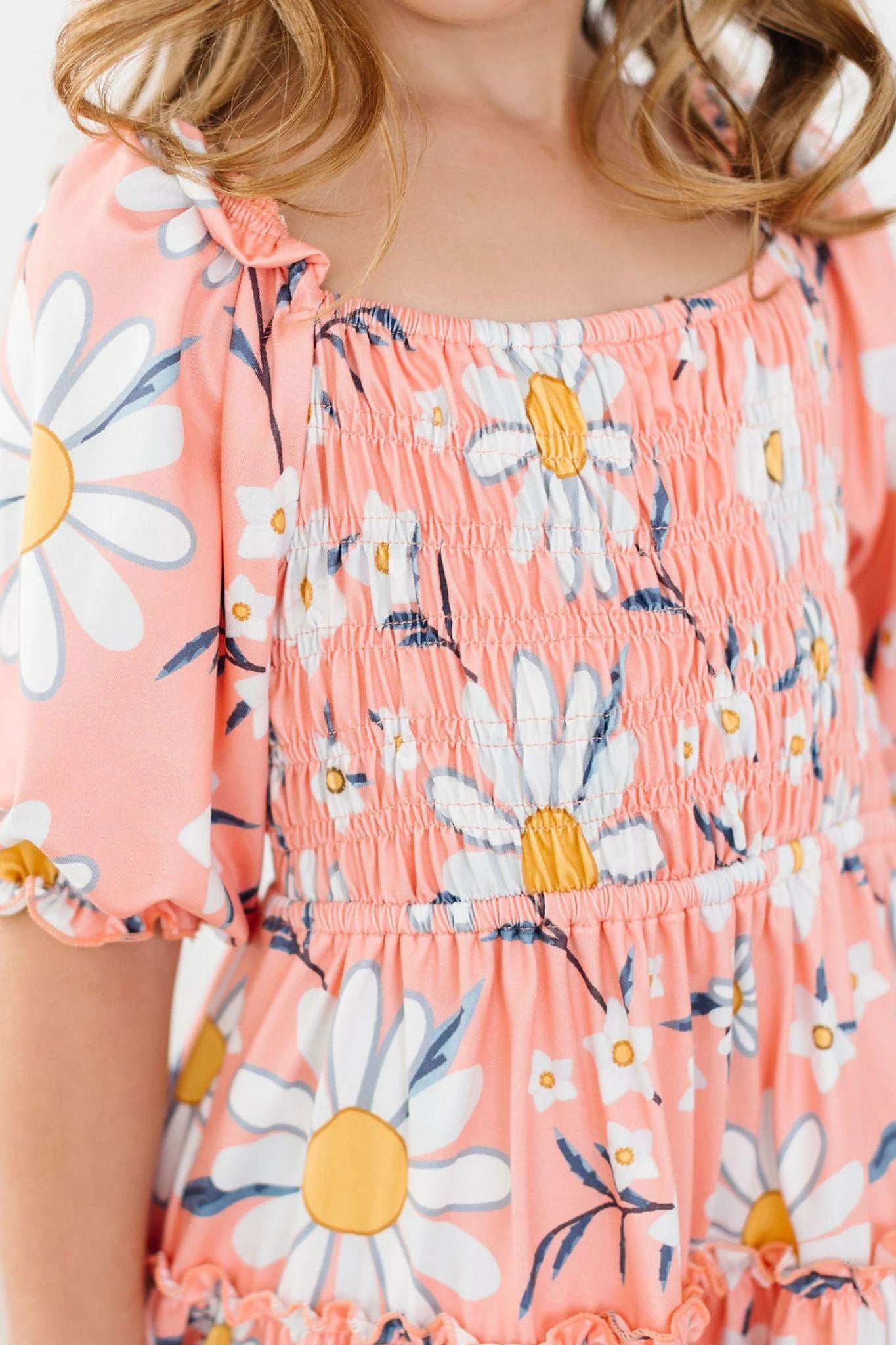 Close-up of a child wearing a pink floral dress with daisy pattern on a white background
