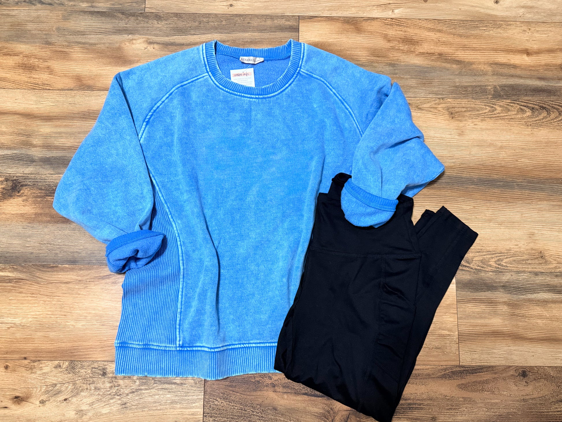 Blue sweatshirt and black leggings on a wooden surface