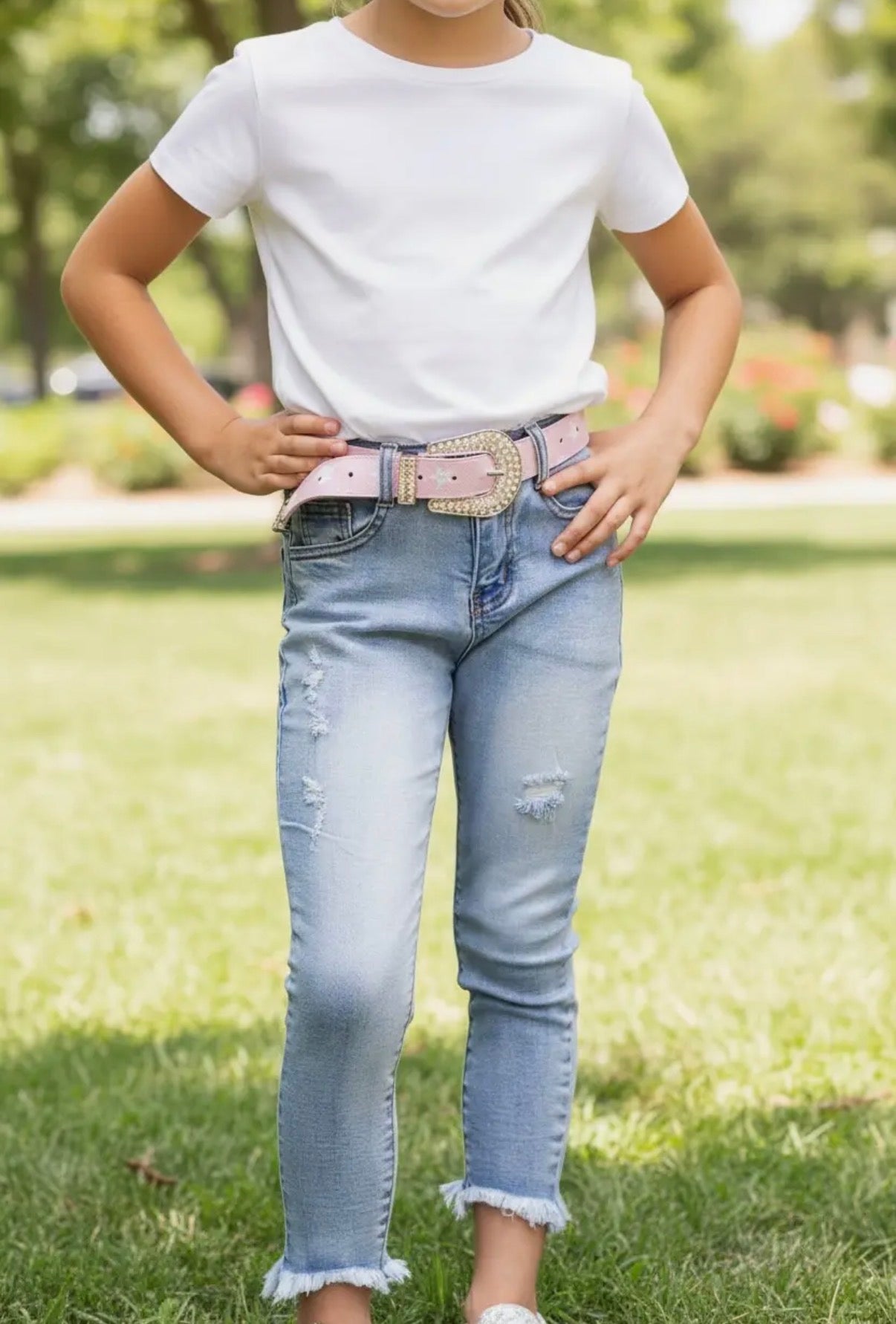 Person wearing a white t-shirt and light blue jeans with a decorative belt in an outdoor setting.
