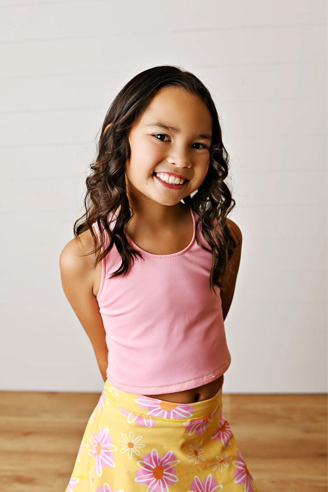 Young girl wearing a pink top and yellow floral skirt against a plain background