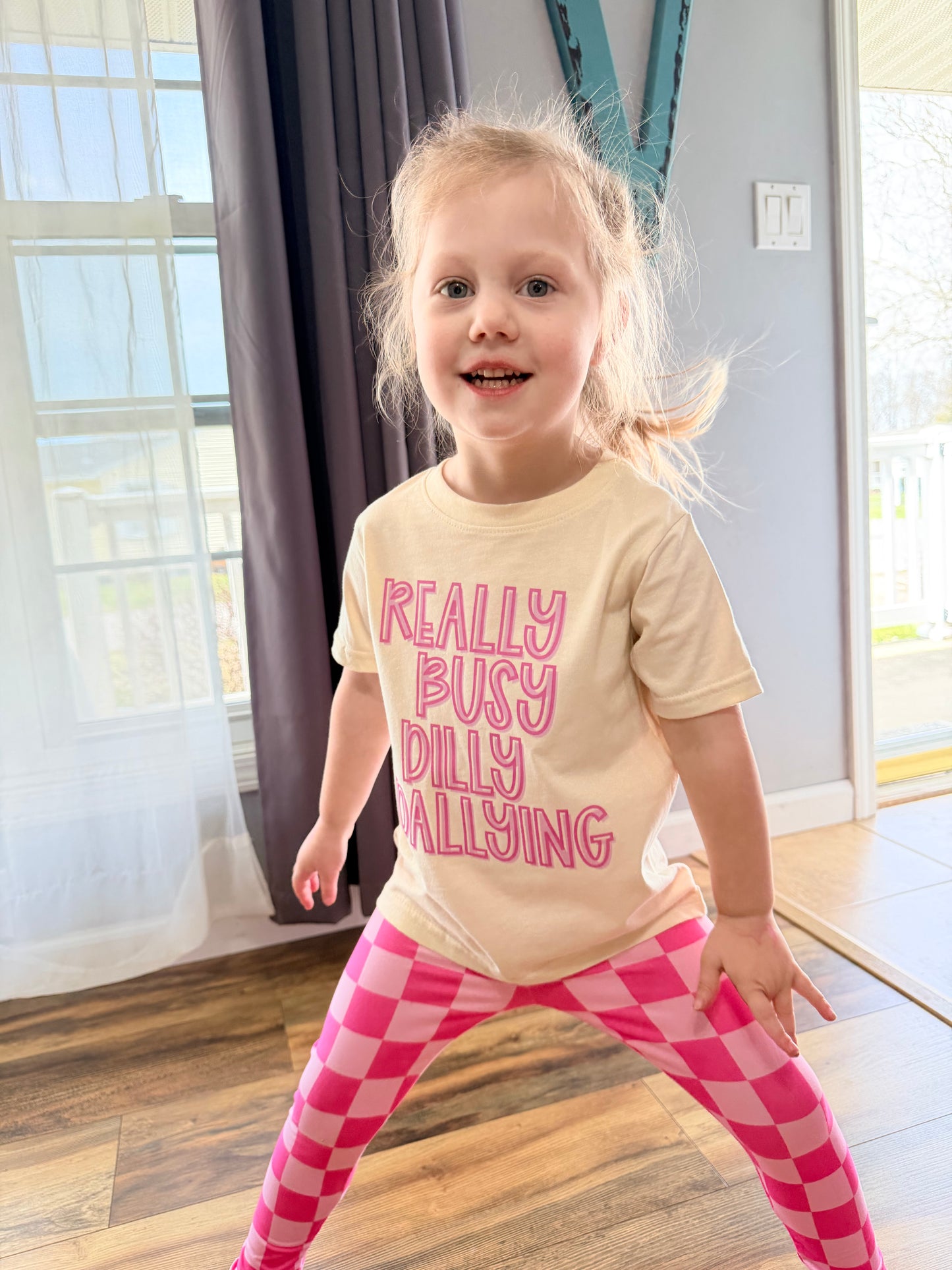 Child wearing a shirt with text in a room with large windows