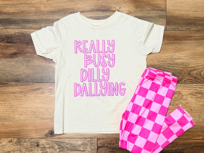 White t-shirt with pink text and pink checkered leggings on a wooden surface