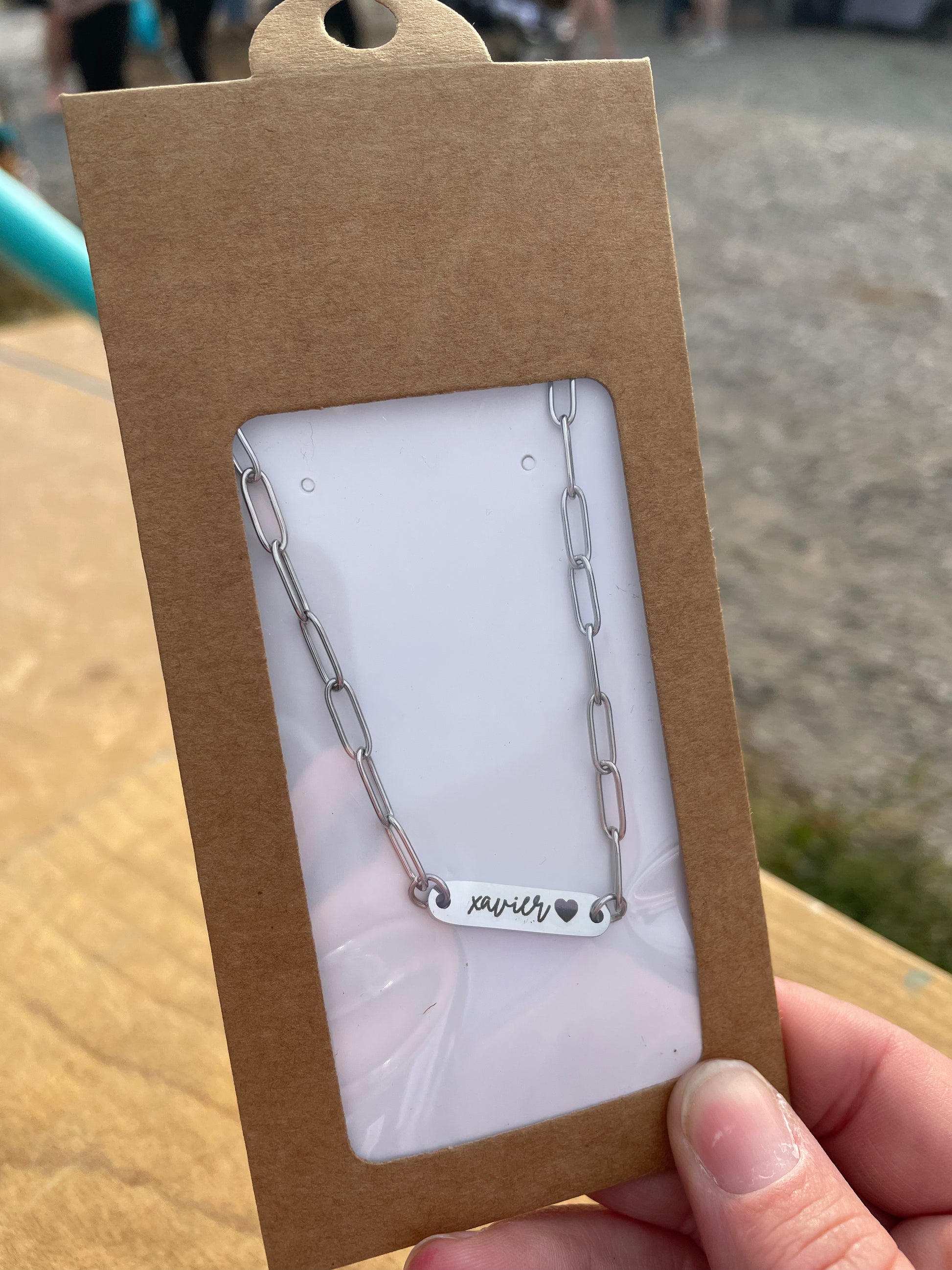 Silver chain necklace with engraved text on a brown card, held by a hand.