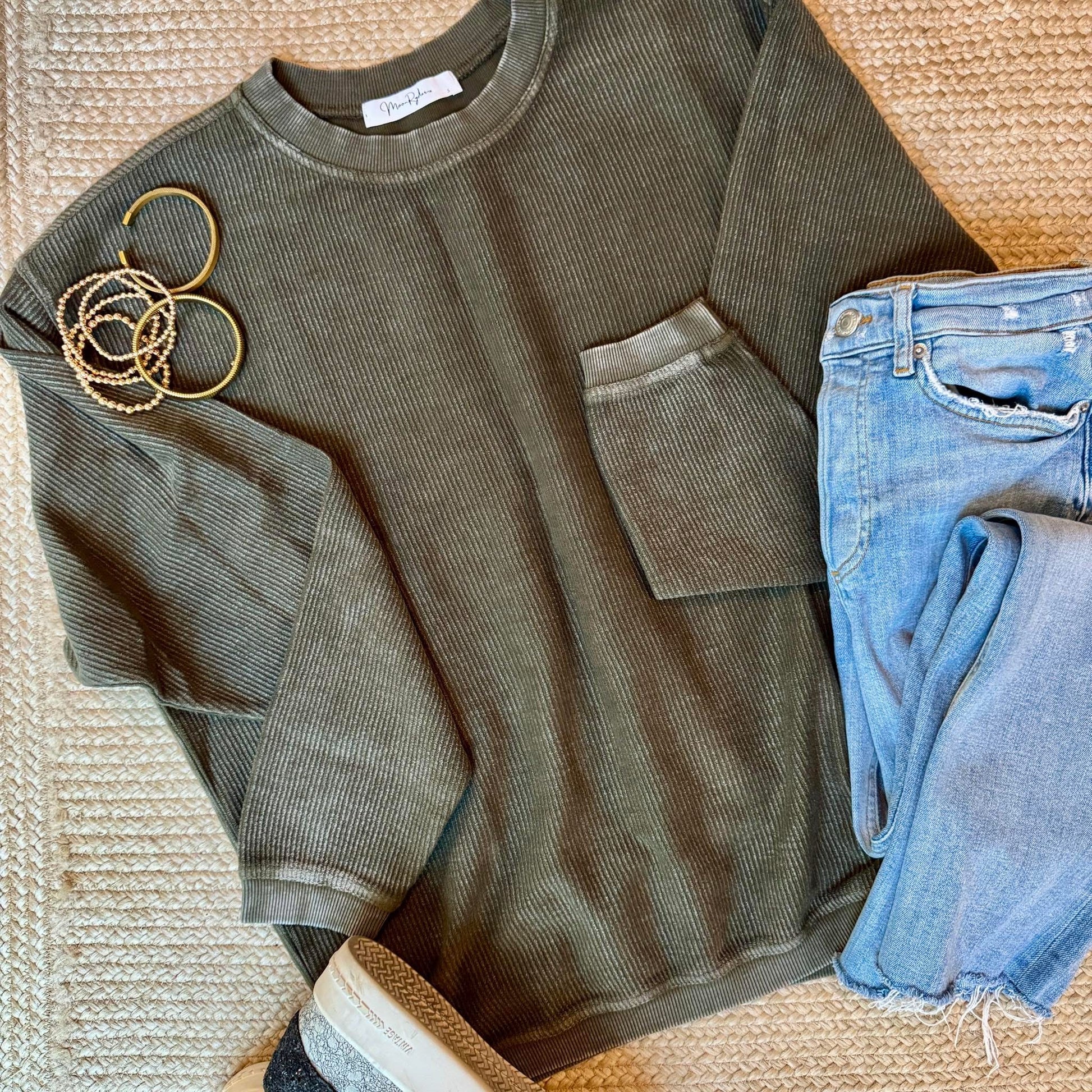 Hunter green corded crew and blue jeans on a textured surface