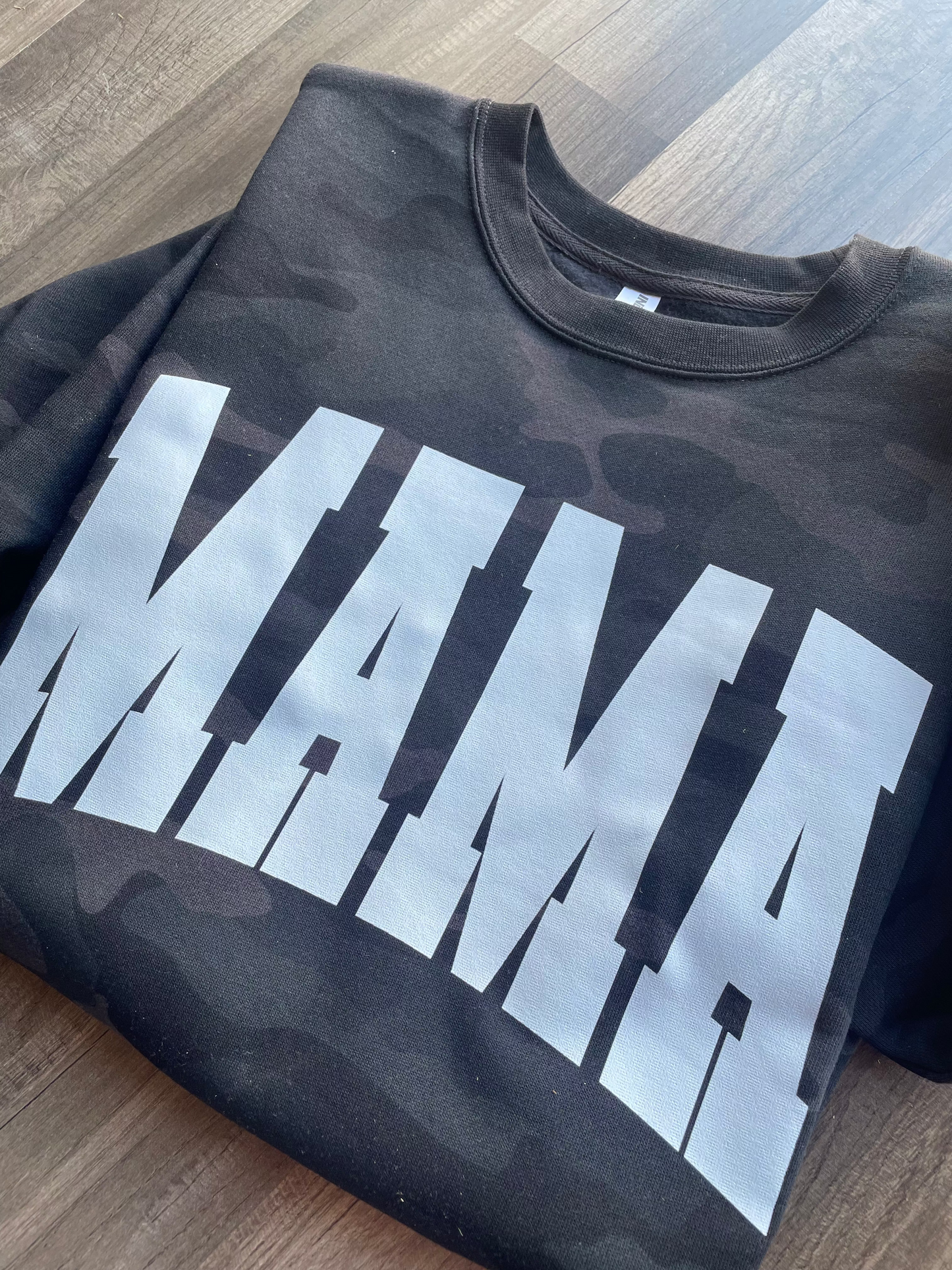 Black camouflage sweatshirt with 'MAMA' printed in white on a wooden surface