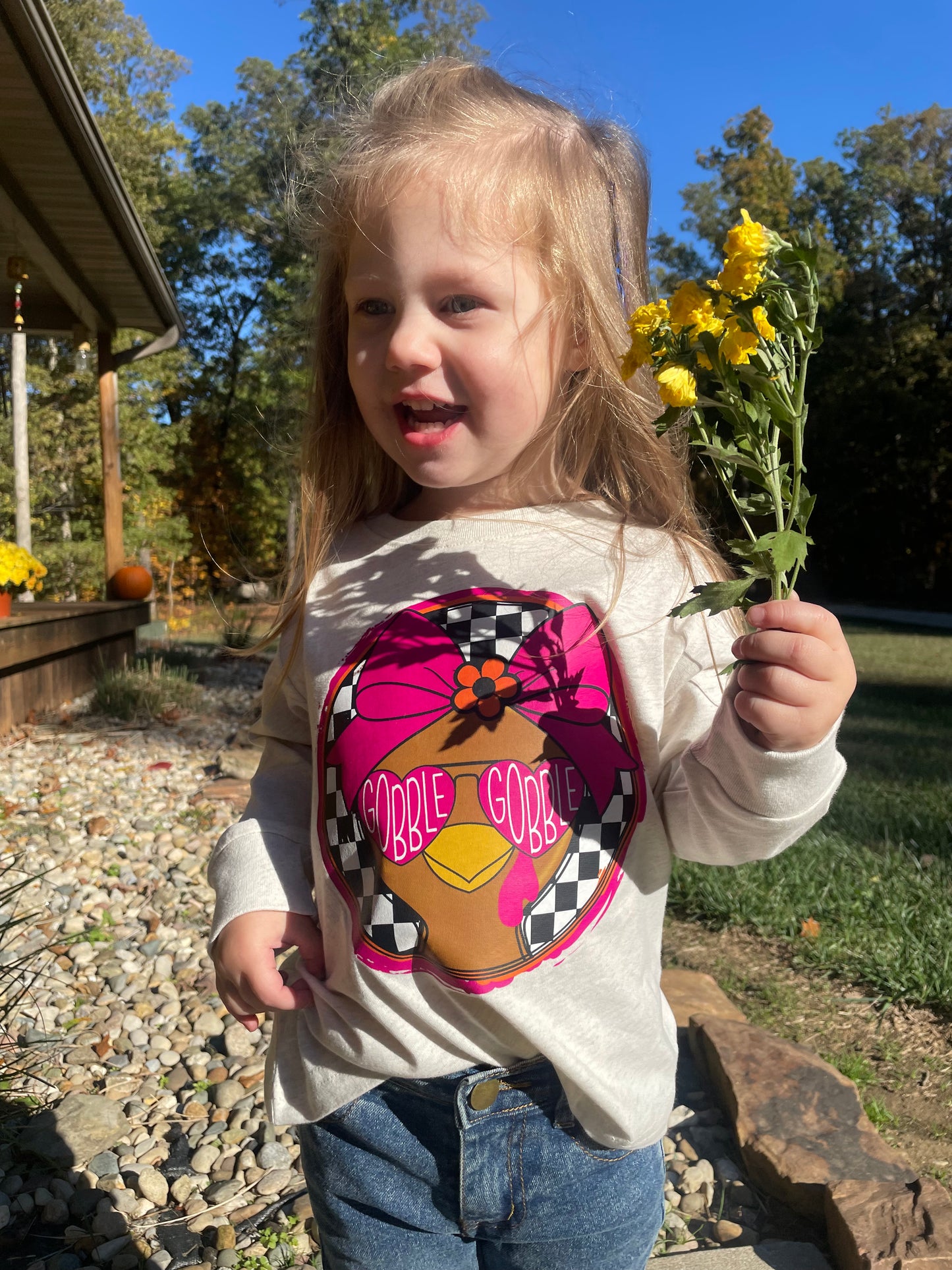 Child wearing thanksgiving graphic shirt holding flowers outdoors