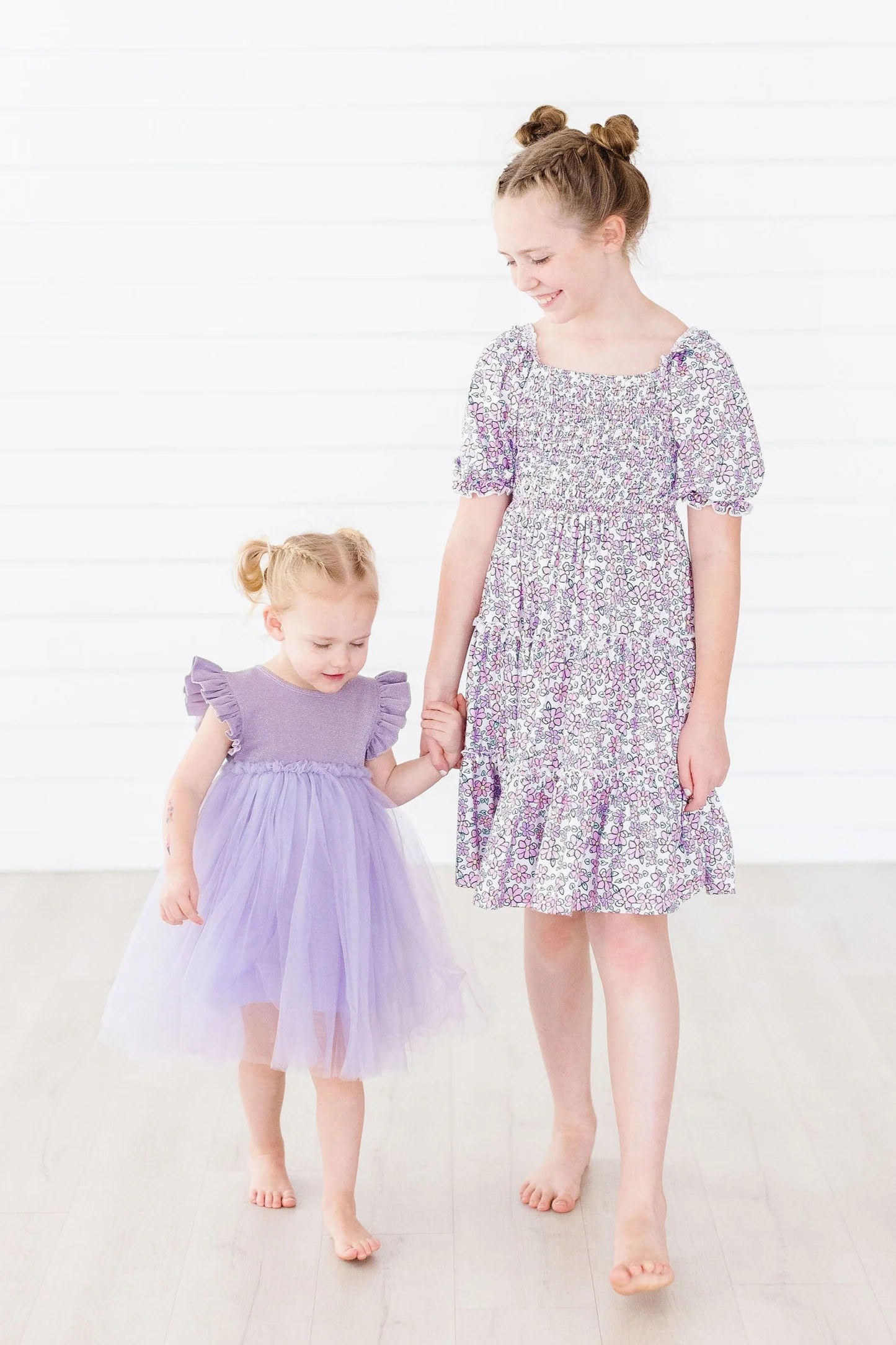 Two young girls wearing matching purple dresses on a white background