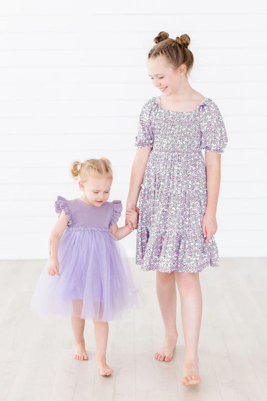 Two young girls wearing matching purple dresses on a white background