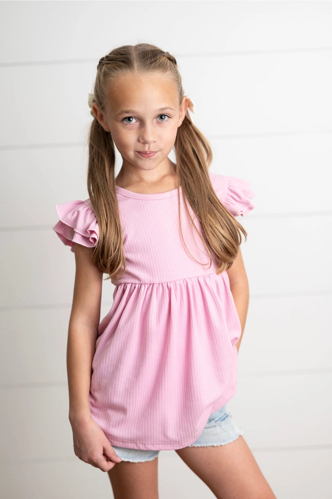 Young girl wearing a pink shirt with ruffled sleeves against a white background
