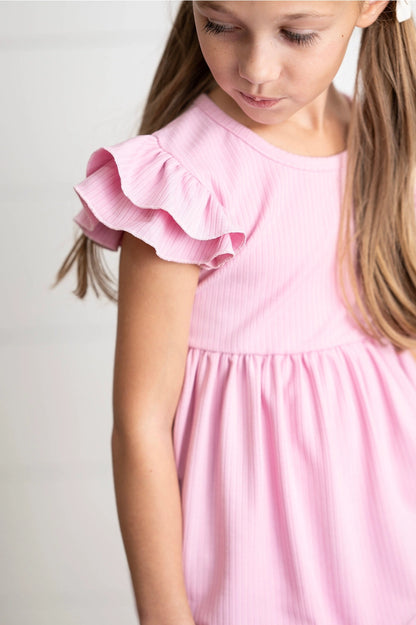 Young girl wearing a pink shirt with ruffled sleeves against a plain background