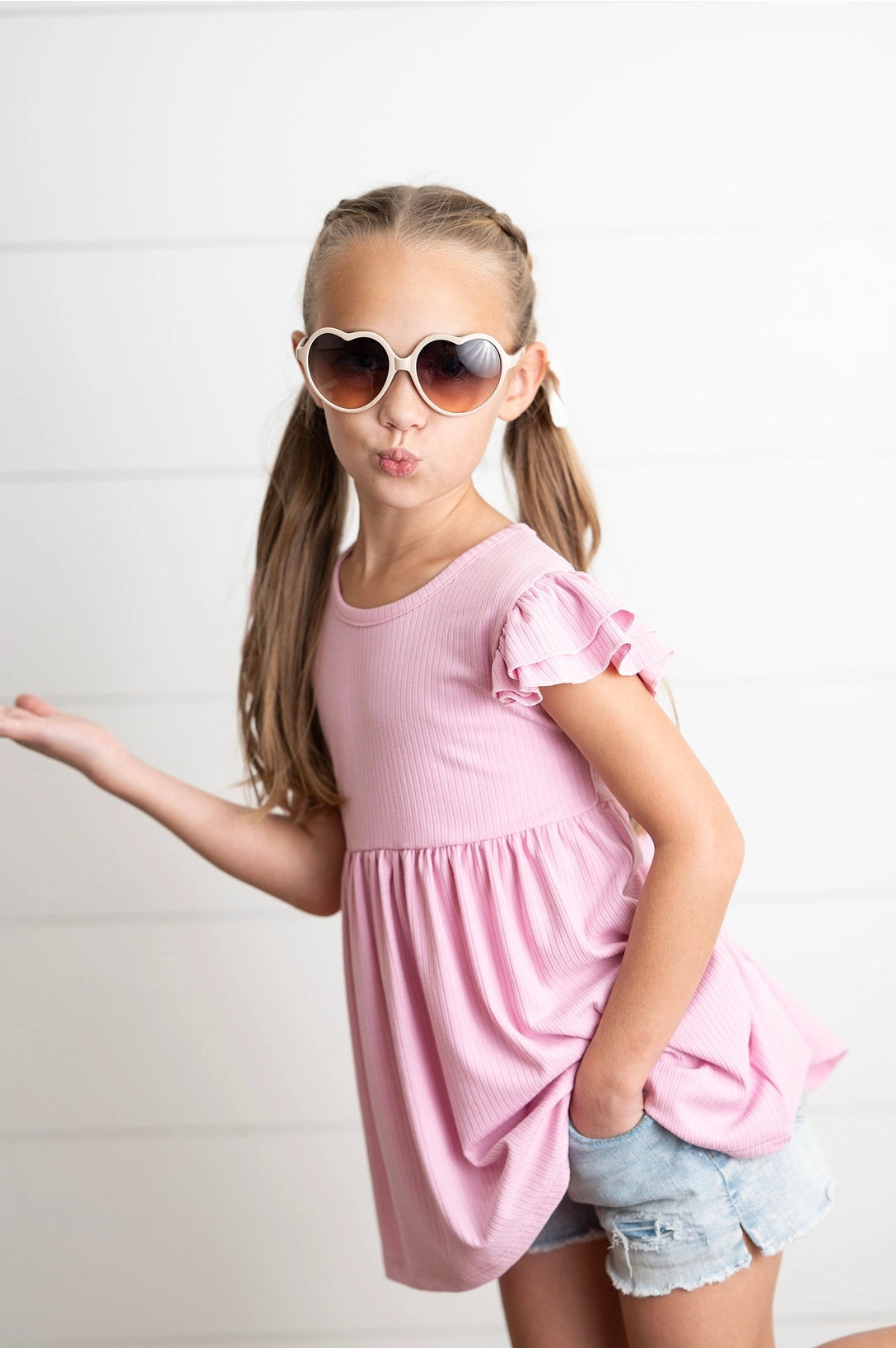 Young girl wearing a pink shirt and heart-shaped sunglasses on a white background