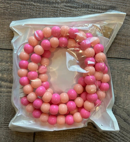 Pink and coral beaded charger in a clear plastic bag on a wooden surface