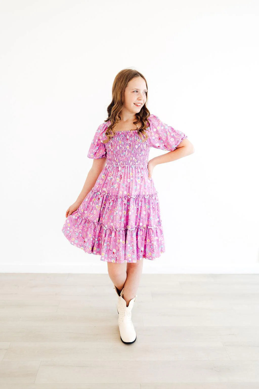 Young girl wearing a purple floral dress with white boots on a light background