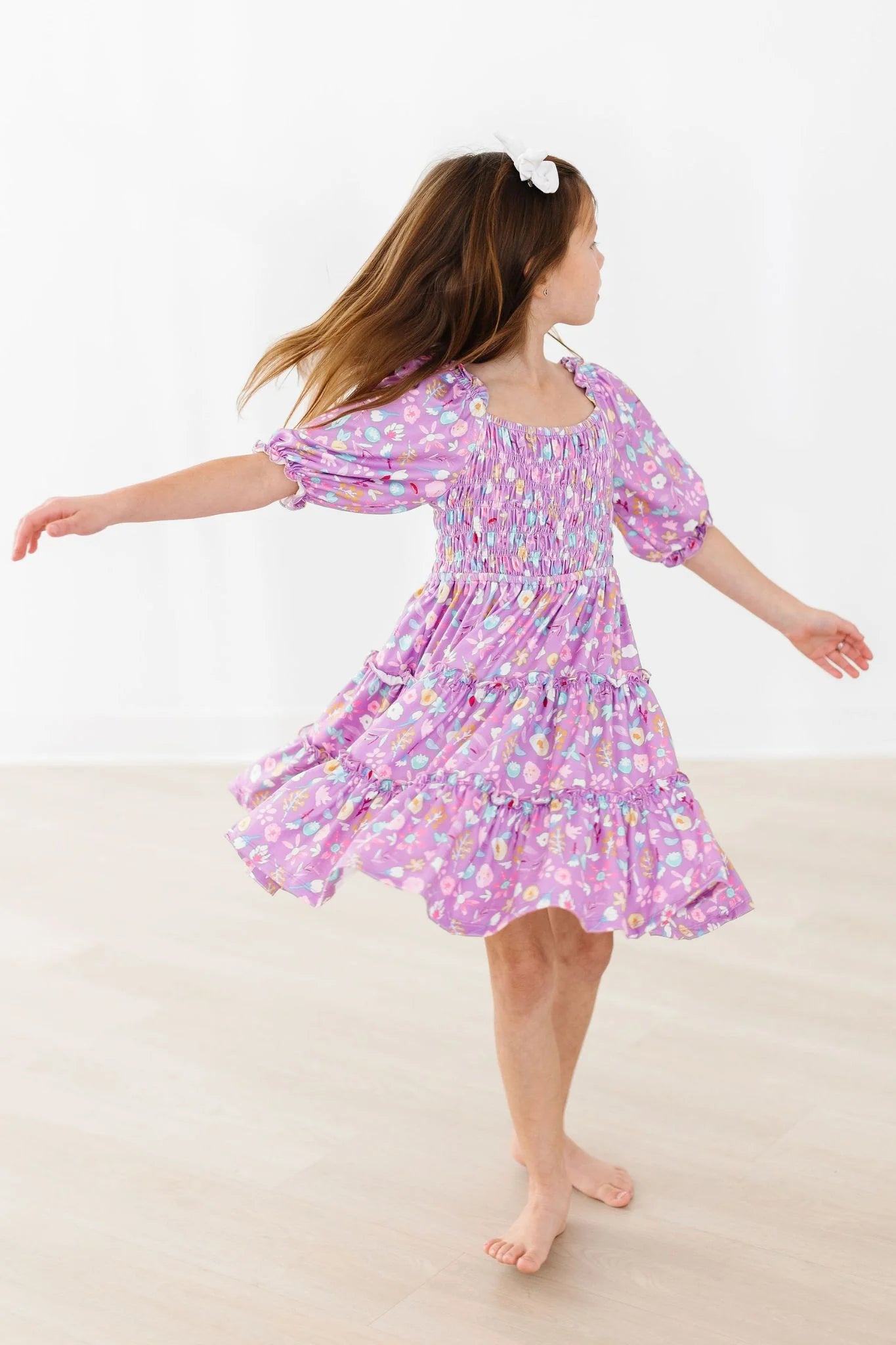 Young girl in a purple floral dress standing on a white background