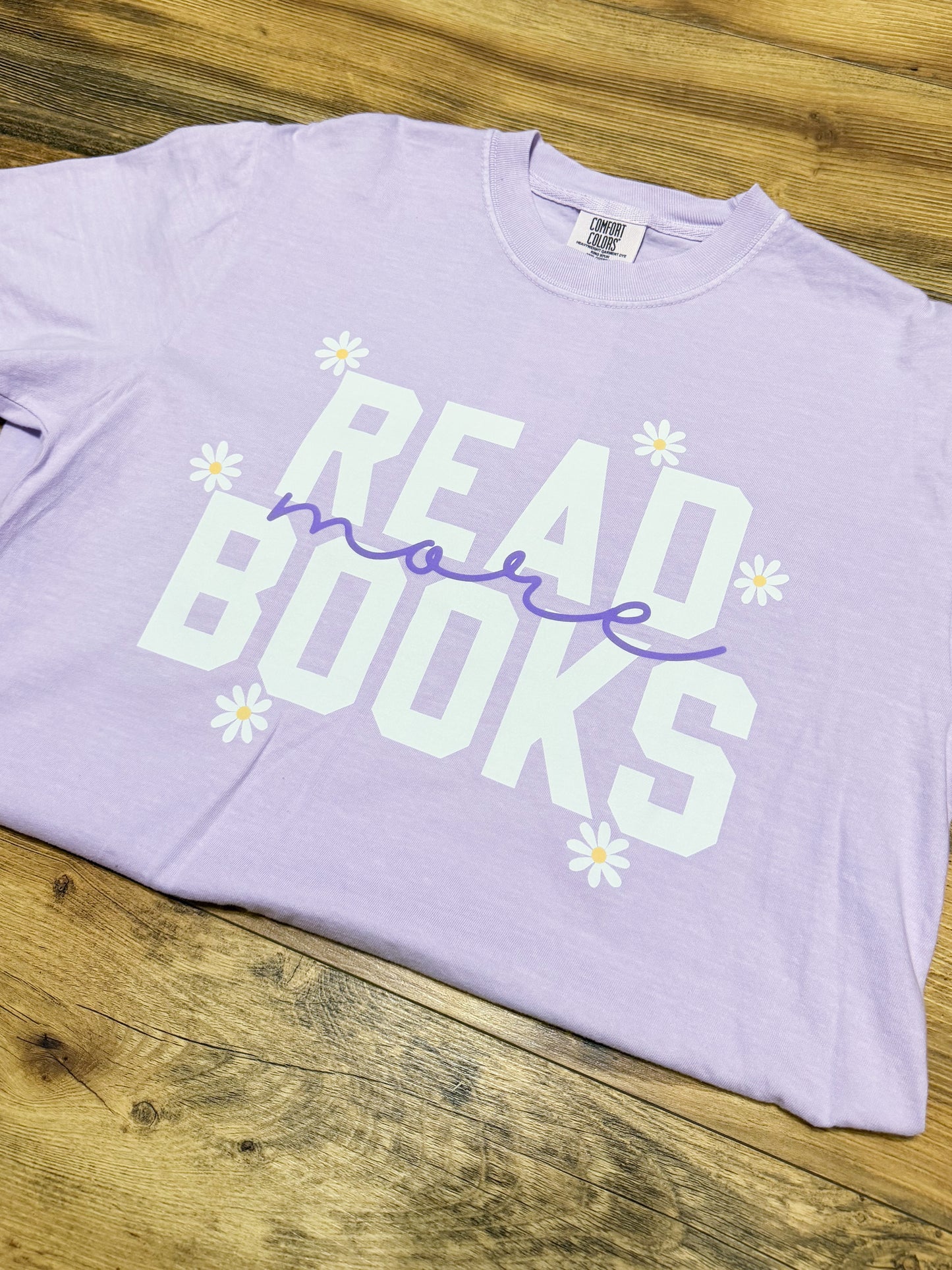 Lavender t-shirt with 'Read more books' text on a wooden surface