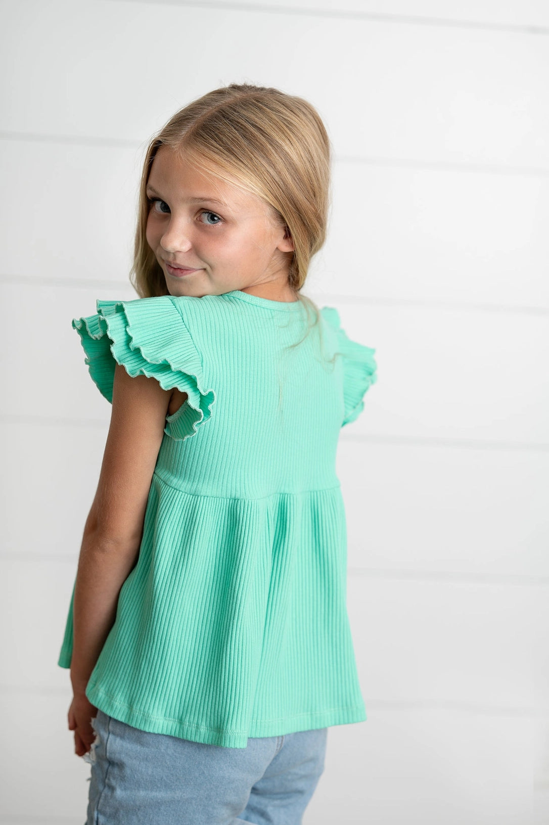 Young girl wearing a turquoise blouse with ruffled sleeves on a white background