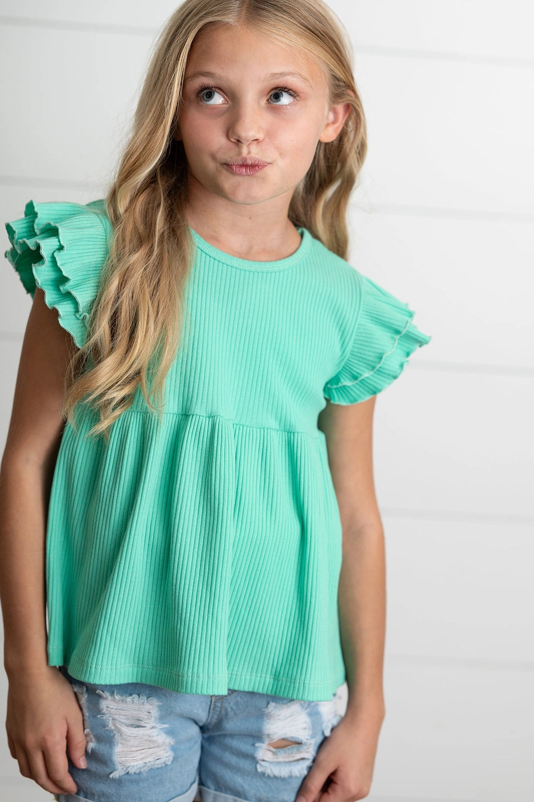 Young girl wearing a turquoise ruffled top against a white background