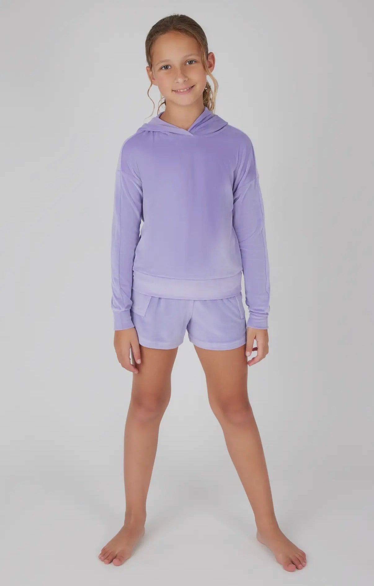 Young girl wearing a purple hoodie and shorts set on a white background