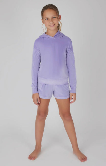 Young girl wearing a purple hoodie and shorts set on a white background