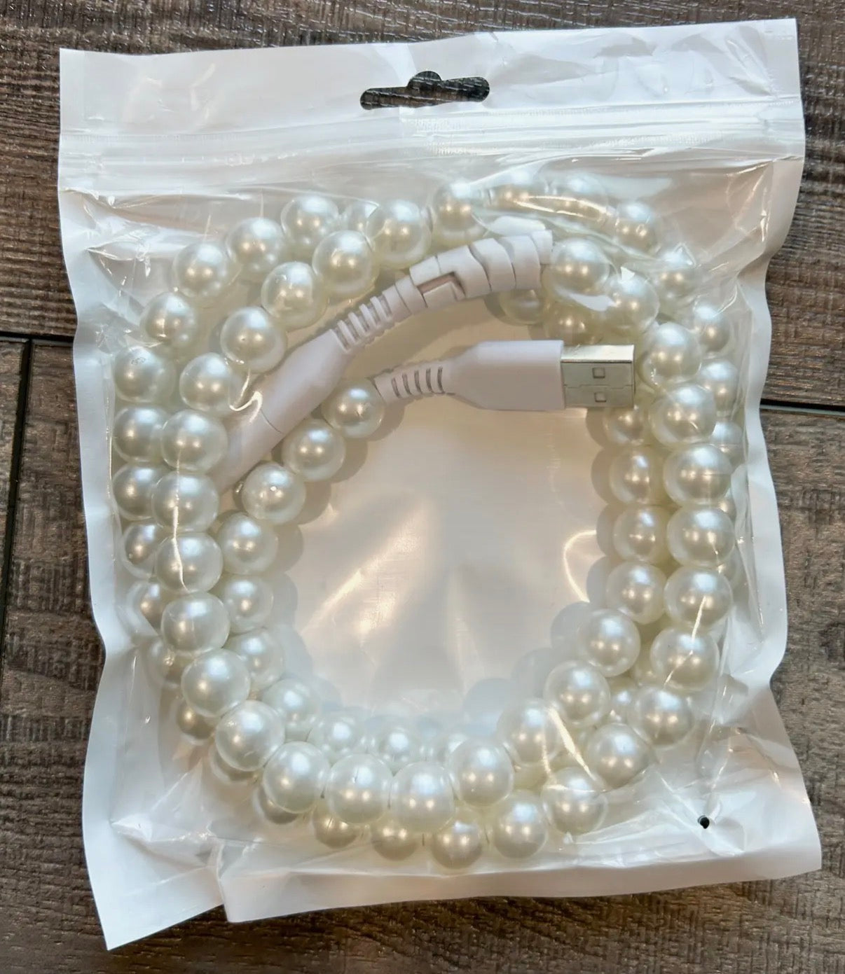 Pearl-colored USB cable coiled inside a clear plastic bag on a wooden surface