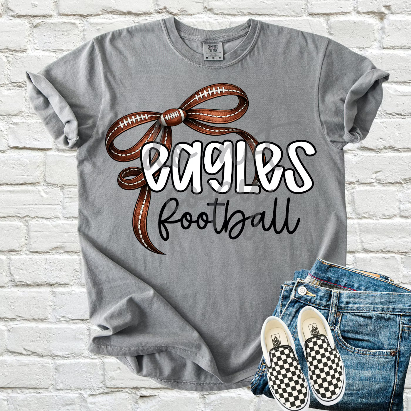 Gray t-shirt with 'Eagles Football' design, checkered shoes, and jeans on a brick wall background